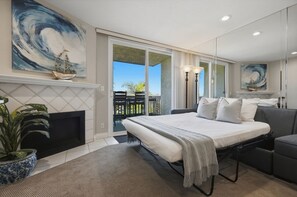 A bedroom with a bed, a sofa, a fireplace, and a balcony with a view.