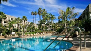 A resort pool with clear blue water, surrounded by palm trees and lounge chairs.