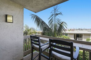 A balcony with two wooden chairs and a table, overlooking a marina with boats and palm trees.
