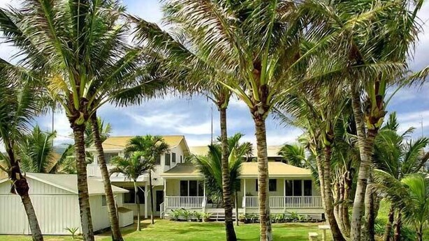 A two-story house with a porch, surrounded by palm trees and a well-maintained lawn.