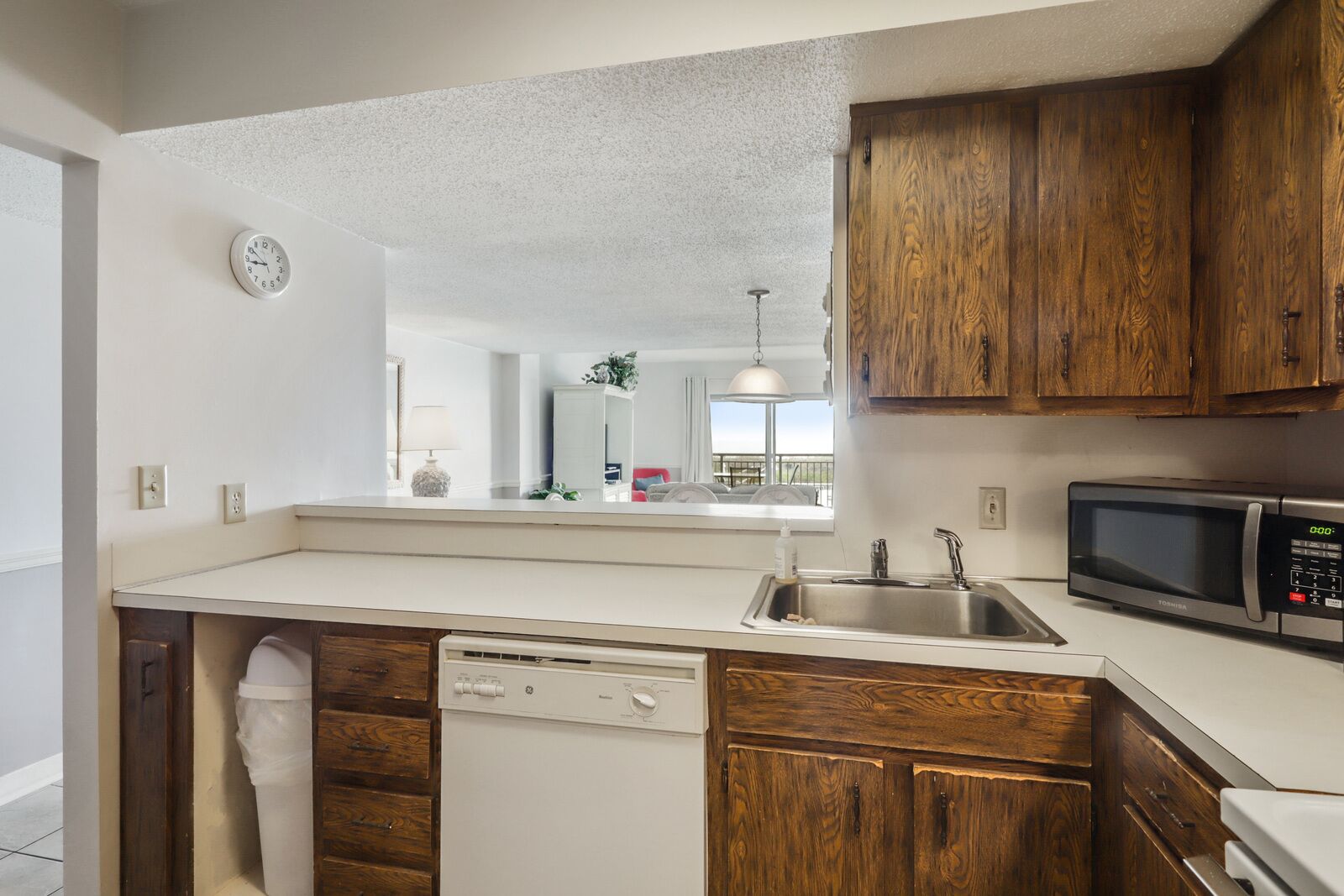 A compact kitchen with wooden cabinets, a built-in dishwasher, a stainless steel sink, and a microwave.