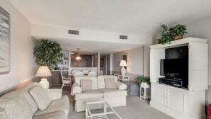 En moderne stue med en sofa, et fjernsyn og et spiseområde i baggrunden.