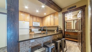 A kitchen with wooden cabinets, a stainless steel sink, a microwave, and a built-in oven. There are three bar stools and a rug on the floor. - Walk to Ski Condo, Pool, Spa, Gym, Tennis 398 (Mammoth Lakes)