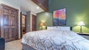 A bedroom with a large bed, two bedside lamps, a painting on the wall, and a wooden door. - Walk to Ski Condo, Pool, Spa, Gym, Tennis 398 (Mammoth Lakes)