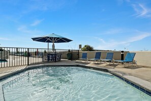A swimming pool with a tiled edge, a fenced area, and blue lounge chairs.