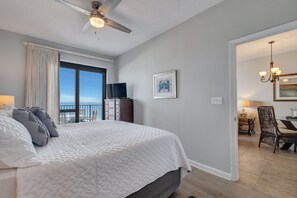 A bedroom with a large bed, a ceiling fan, a TV, and a view of the ocean.