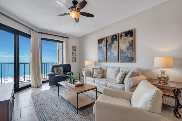 A living room with a view of the beach, a ceiling fan, a large world map artwork, and a lamp.