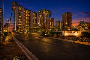A multi-story hotel with illuminated balconies, a parking lot, and a sign indicating the name 'PHOENIX VI-VII'.