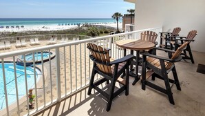 A balcony with wooden chairs and a table, overlooking a pool and a beach. - Summer Place 207 - 3 BR Beach Condo - 2 Sets of Beach Service! (Fort Walton Beach)