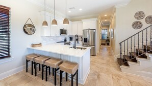 A modern kitchen with a central island, pendant lights, and a stainless steel refrigerator.