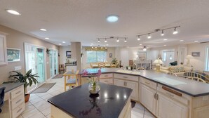 A spacious kitchen with a central island, a dining area with chairs, and a living area with a sofa and lamp. - Newmans Beachview 3 bedrooms, 3 bathrooms (Jekyll Island)