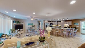 A spacious living room with a sofa, chairs, a TV, and a dining area with a bar. - Newmans Beachview 3 bedrooms, 3 bathrooms (Jekyll Island)