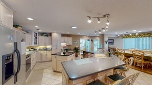 A spacious kitchen with a central island, wooden cabinets, and a dining area with chairs and a table. - Newmans Beachview 3 bedrooms, 3 bathrooms (Jekyll Island)