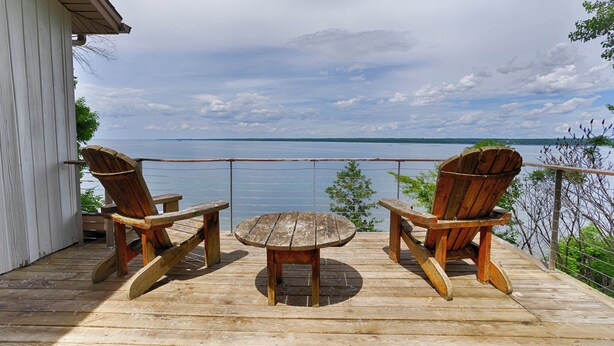 En træterrasse med to Adirondack-stole og et lille bord, med udsigt over vandet.