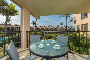A glass table with four teacups and saucers, surrounded by chairs, on a balcony with a view of palm trees and buildings. - Kamaole Sands #2-301 Great Location Near Beach,Fitness Center,Hot Tub, A/C! (Kihei)