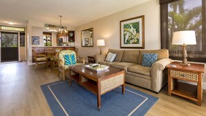 A living room with a sofa, coffee table, and dining area with chairs and a table. - Kamaole Sands #2-301 Great Location Near Beach,Fitness Center,Hot Tub, A/C! (Kihei)