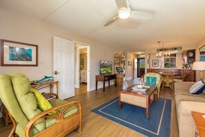 A spacious living room with a large window, a dining area with a wooden table and chairs, and a kitchen area with a countertop and cabinets.