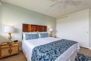 A bedroom with a bed, two bedside tables, a nightstand, a ceiling fan, and a door.