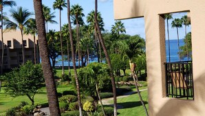 A hotel courtyard with palm trees, a view of the ocean, and a building with a balcony. - Kamaole Sands #2-301 Great Location Near Beach,Fitness Center,Hot Tub, A/C! (Kihei)