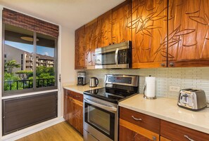 A modern kitchen with a microwave, stove, and toaster, wooden cabinets, and a view of a building through a window.
