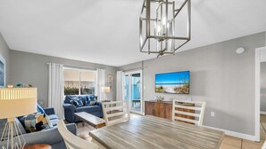 Ein modernes Wohnzimmer mit Essbereich, einer Sofagarnitur, einem Fernseher und Blick ins Freie.