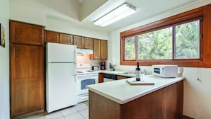 Una cocina con armarios de madera, un refrigerador blanco, una estufa, un microondas y una ventana con vistas a árboles.