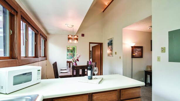 Una cocina con microondas blanco, armarios de madera y un comedor con mesa y sillas.