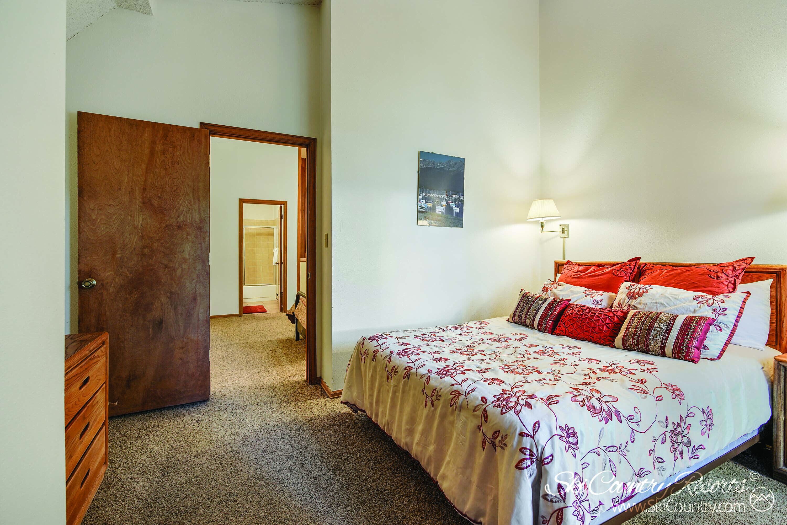 Une chambre à coucher avec un lit, une commode en bois, une porte et une lampe fixée au mur.