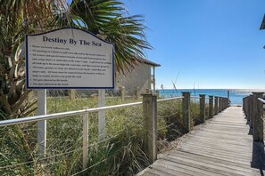 A wooden boardwalk leading to a beach with a sign titled 'Destiny By The Sea' listing beach rules.