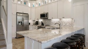 Una cocina moderna con armarios blancos, un refrigerador de acero inoxidable, un microondas, una estufa y una isla grande con taburetes de bar.