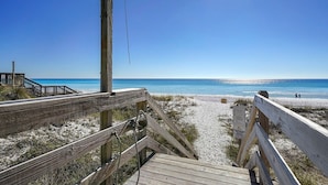 Un paseo marítimo de madera que lleva a una playa con cielos despejados y el océano al fondo.