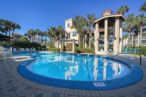 A swimming pool with a 3 FT depth marker, surrounded by palm trees and a building with a covered patio area.