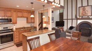 Una cocina moderna con encimeras de granito, armarios de madera y electrodomésticos de acero inoxidable. Hay un comedor con mesa y sillas de madera.