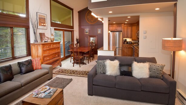 Un salón amplio con un sofá de color gris oscuro, un aparador de madera y un comedor con una mesa y sillas de madera.