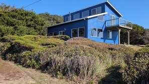 A modern two-story house with a balcony, surrounded by lush greenery and hills.