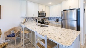 A kitchen with white cabinets, a stainless steel refrigerator, a microwave, and a sink. - Gulf Front Condo, 3rd level, Amazing Views - Near shops/restaurants (Santa Rosa Beach)