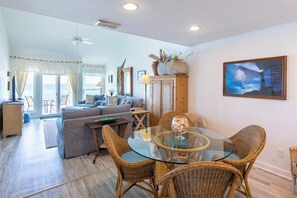 A spacious living area with a glass-top dining table surrounded by wicker chairs, a sofa set, and a view to the outside. - Whispering Sands #301 - Gulf Front Condo on Private Dune Allen Beach! (Santa Rosa Beach)