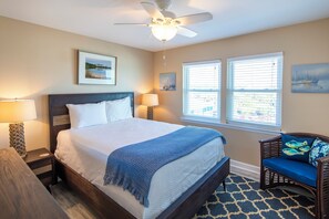 A bedroom with a bed, two bedside lamps, a ceiling fan, and two windows with blinds.