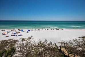 A beach with clear skies, sandy shore, and a wooden boardwalk leading to the water.