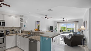 A modern kitchen with white cabinets, a blue island, and a dining area with a sofa and table. - Luxurious Ground Floor Condo: Proximity to Pool, Full Access to Amenities. (Herradura)