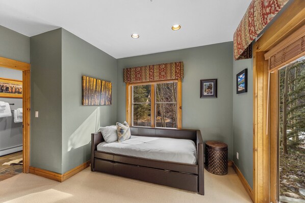 A bedroom with a bed, a window, a painting, and a view of trees. - Spacious Patio w/ Gorgeous Mountain Views in Cozy Condo Near Resort Shuttle (Keystone)
