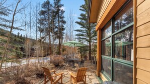 Une terrasse avec une table et des chaises, un parasol vert et une vue sur une zone boisée.