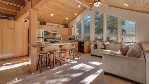 Una cocina amplia con armarios de madera, una isla central con taburetes y grandes ventanales con vistas al exterior.
