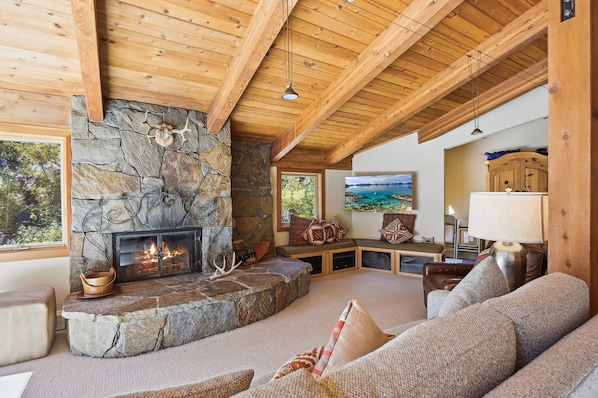A cozy living room with a stone fireplace, wooden ceiling beams, and a comfortable seating area.