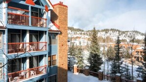 Un edificio de varios pisos con balcones, una chimenea de ladrillo y una montaña nevada al fondo.