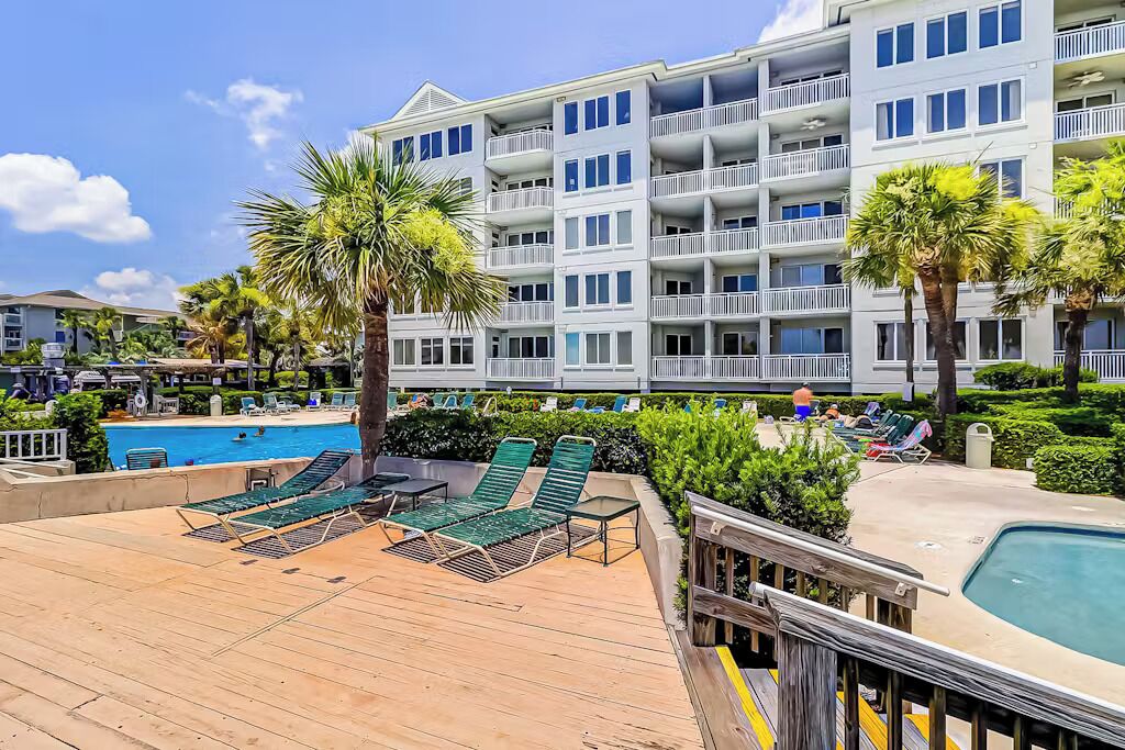 A hotel with a pool area, lounge chairs, and a wooden deck.