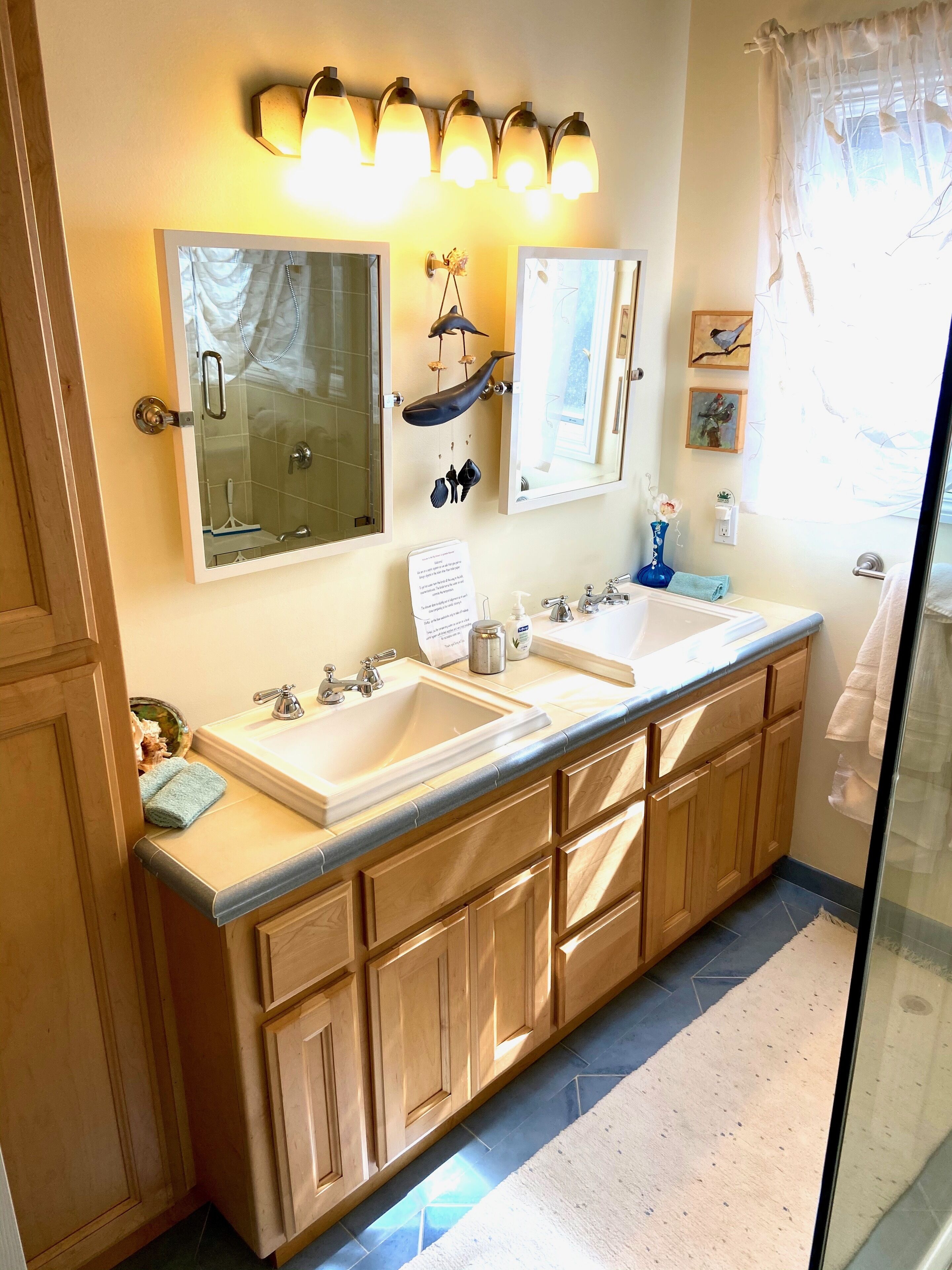 A bathroom with two sinks, wooden cabinets, a mirror, and wall-mounted lights.
