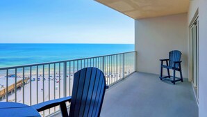 Ein Balkon mit Blick auf Strand und Meer. Zwei Adirondack-Stühle und ein Tisch sind vorhanden.
