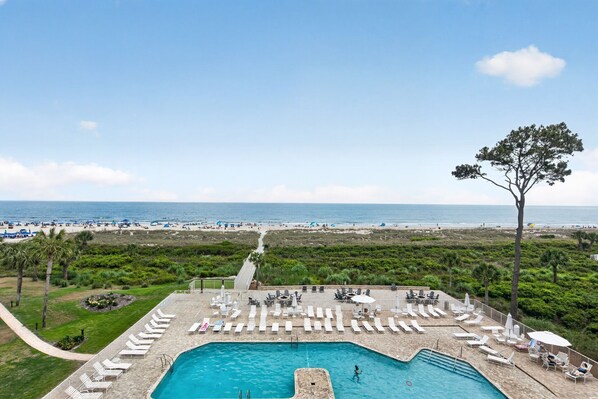 Un espace piscine avec des chaises longues, une piscine et une vue sur la plage et l’océan.