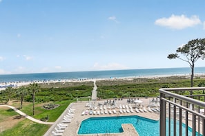 Un espace piscine avec des chaises longues, une vue dégagée sur la plage et un chemin menant à la plage.